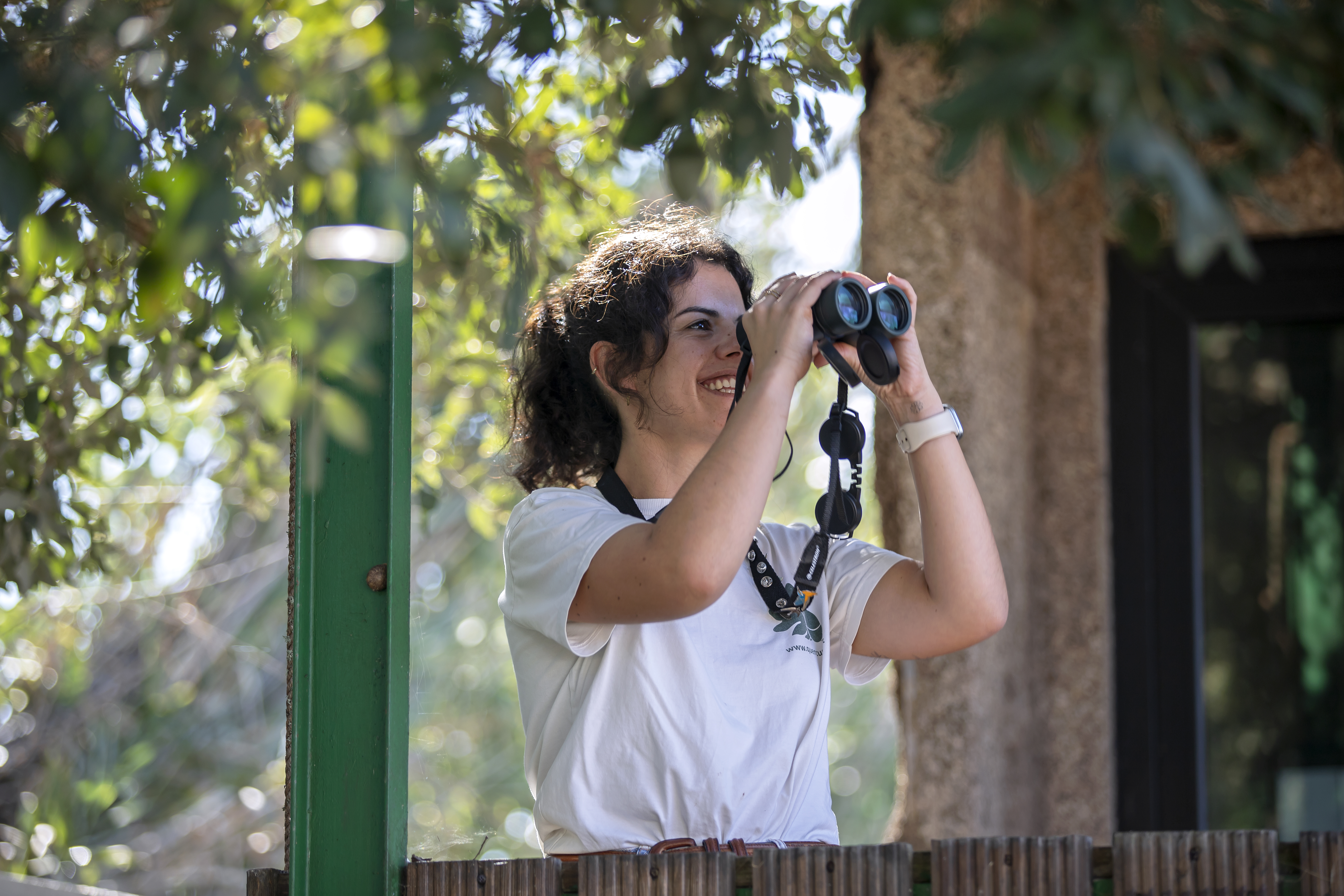 Carolina seguro ao alto os binóculos, tentando ver através deles, dedicando-se à prática de birdwatching