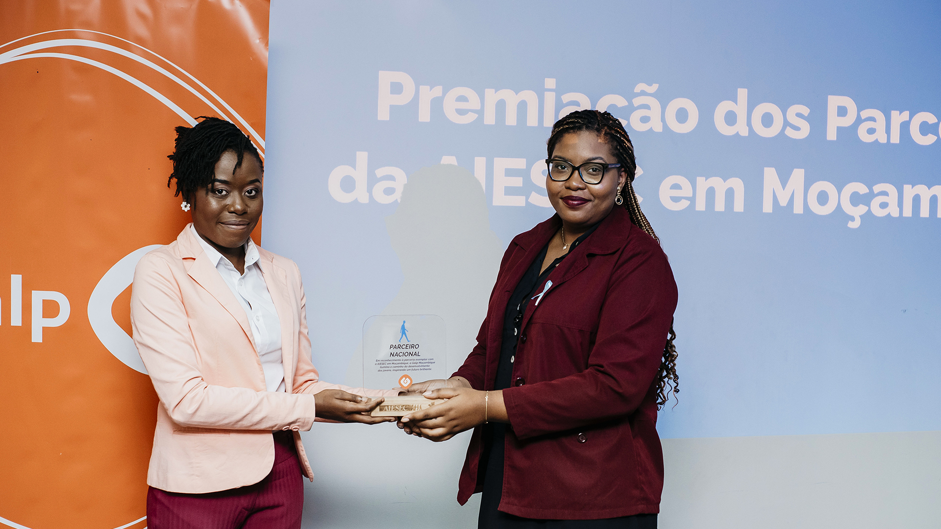 Fotografia de duas mulheres vestidas de forma formal. Ambas seguram num prémio.