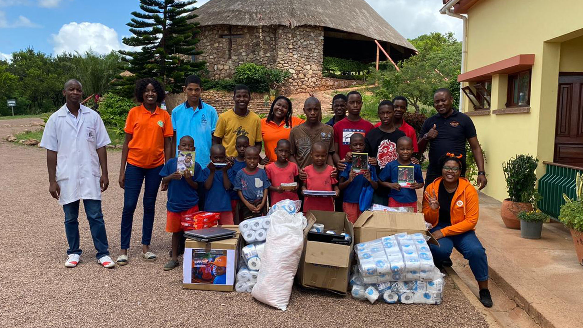 Fotografia de várias pessoas com crianças à sua frente. No chão, à frente das pessoas, vê-se vários materiais.