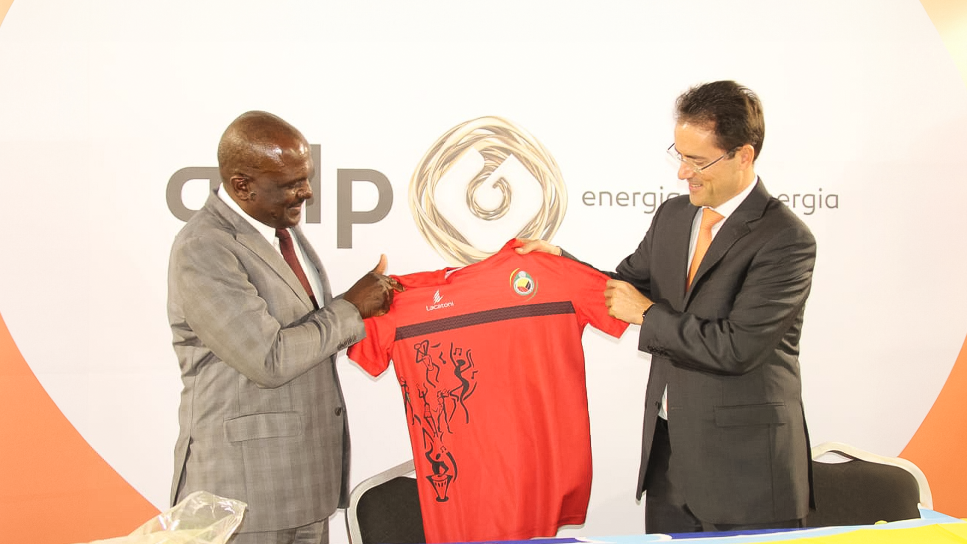 Fotografia de duas pessoas a segurar uma t-shir da Seleção Nacional de Futebol de Moçambique.