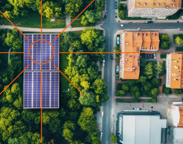Fotografia superior de uma zona urbana. Vê-se várias casa e estradas. Ao lado, uma zona rural com um grande painel solar no meio da vegetação.