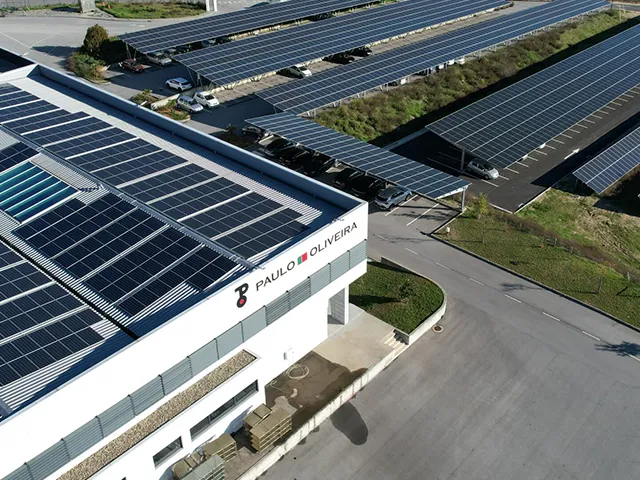 Vista aérea de um complexo empresarial com painéis solares em telhados e coberturas de estacionamento, representando uma comunidade de produção de energia solar partilhada.