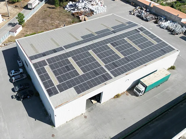 Vista aérea de um complexo empresarial com painéis solares em telhados e coberturas de estacionamento, representando uma comunidade de produção de energia solar partilhada.