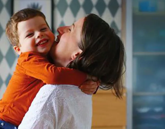 Fotografia de uma senhora com um bebé ao colo, a beijar-lhe a face.